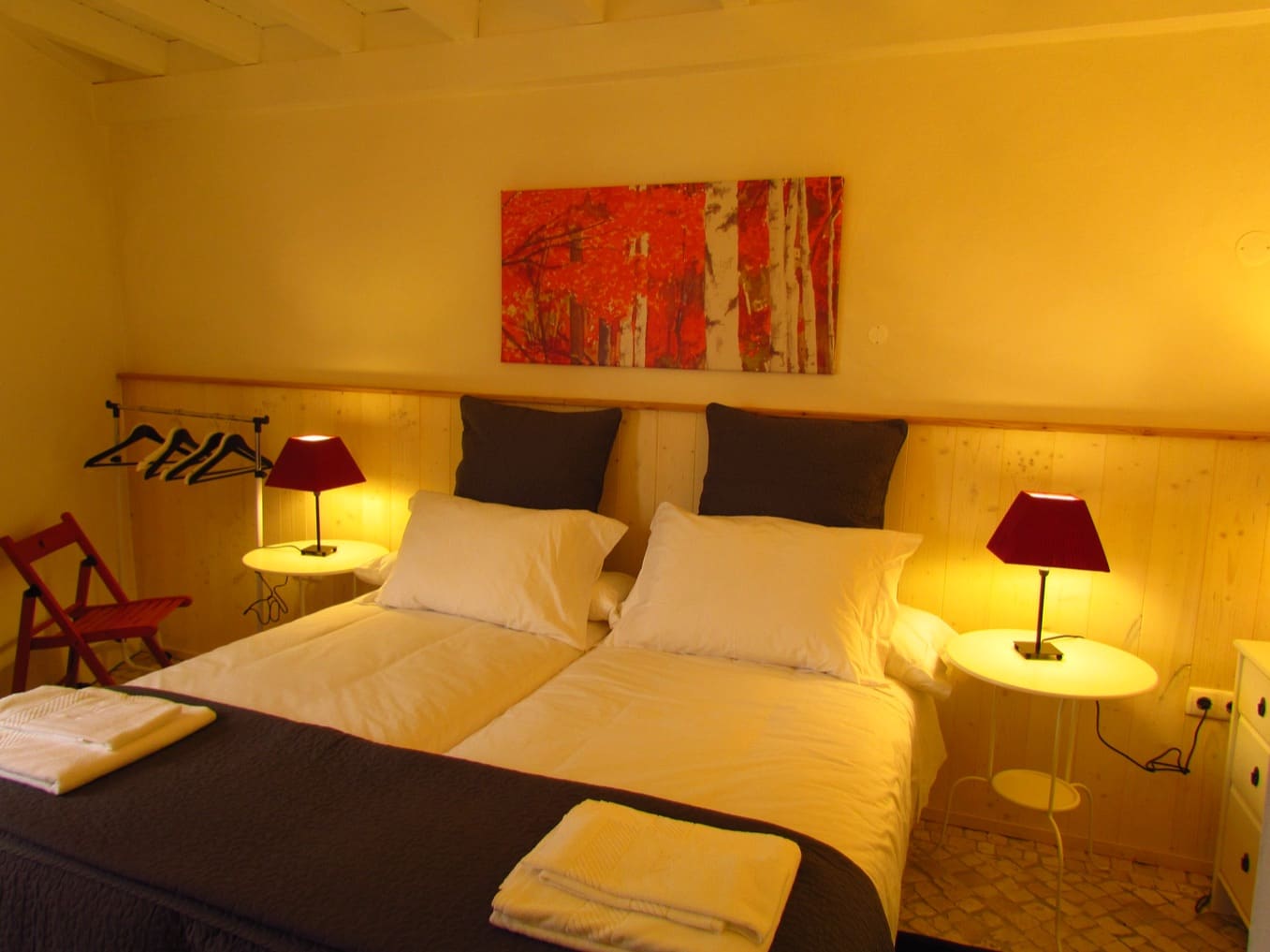Twin beds pushed together under a beamed ceiling, with pine panelling and red bedside lamps