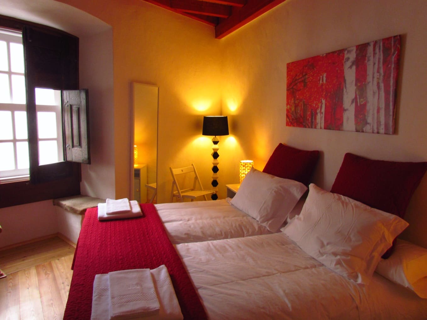 Twin beds below red-painted ceiling beams, beside a window with wooden shutters